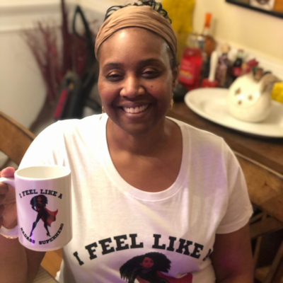 Alicia McCalla smiling holding a I feel like a Badass Superhero Mug and wearing the complementary T-shirt