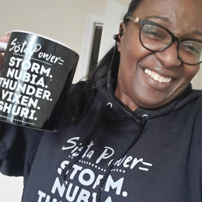 Woman holding Sista Power Mug and Wearing Sweatshirt Storm, Nubia, Thunder, Vixen, and Shuri